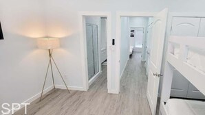 A hallway with a floor lamp, white doors, and a view into a bedroom. - Villas De Laguna 2 3 Bedroom Townhouse (South Padre Island)