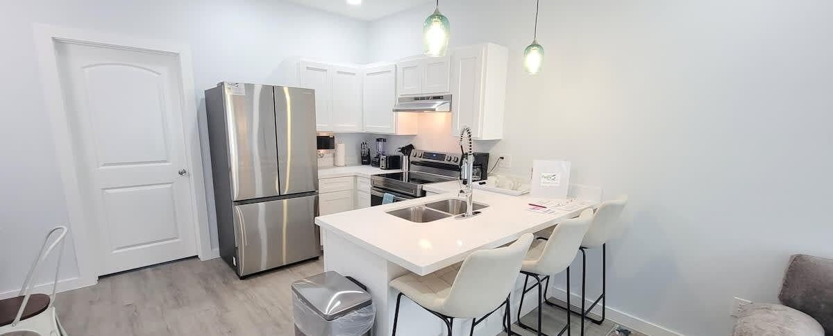 A modern kitchen with a stainless steel refrigerator, white cabinetry, and a central island with bar stools.