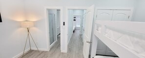 En hall med en golvlampa, vita dörrar och utsikt in i ett sovrum.