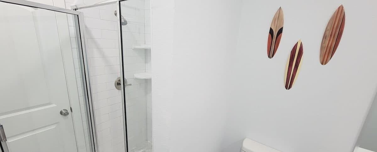 Une salle de bain avec une douche à parois de verre, des toilettes et trois œuvres d’art en bois accrochées au mur.