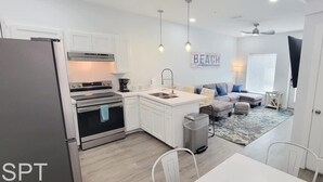 A modern kitchen with white cabinets, stainless steel appliances, and a dining area with a white table and chairs. - Villas De Laguna 3 3 Bedroom Townhouse (South Padre Island)