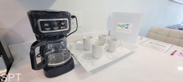 Une machine à café dotée d’un écran numérique, un plateau avec six tasses blanches et une pancarte portant l’inscription « Padraig’s Tea ».