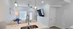 A modern kitchen with a large island, a dining area with a sofa, and a TV mounted on the wall. - Villas De Laguna 3 3 Bedroom Townhouse (South Padre Island)