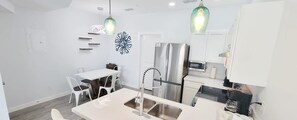 A modern kitchen with white cabinetry, a stainless steel refrigerator, a double sink, and pendant lighting. - Villas De Laguna 3 3 Bedroom Townhouse (South Padre Island)