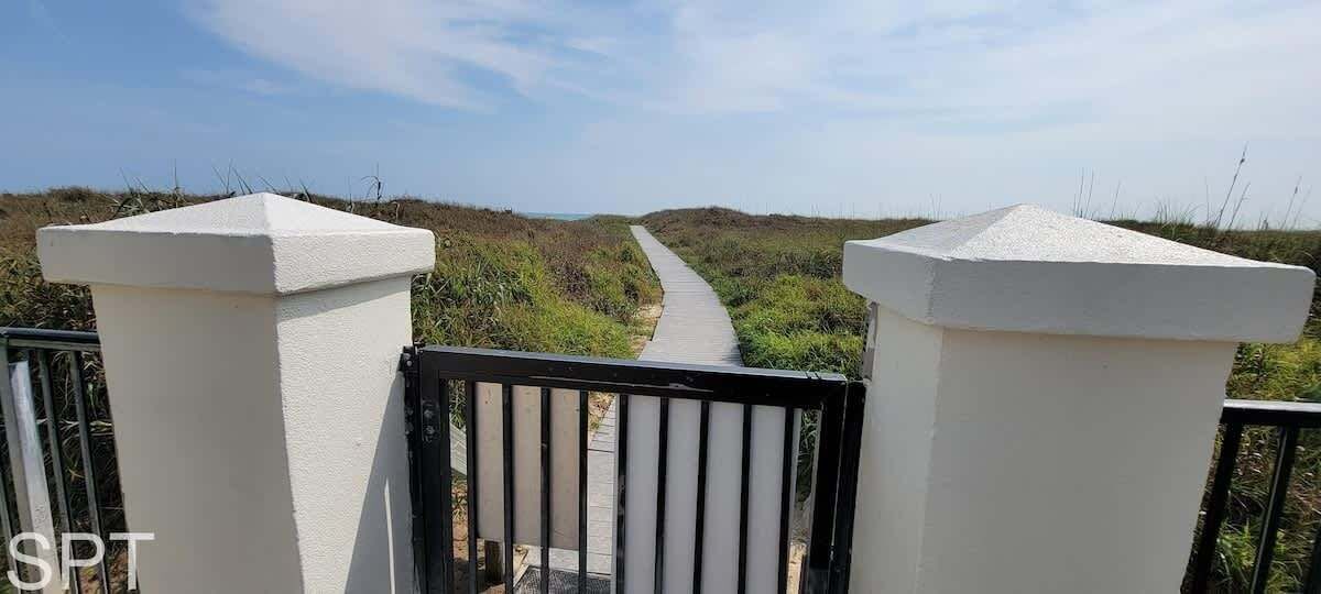 A pathway leading through a natural landscape, flanked by white pillars and a black gate.