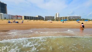 Una playa con edificios al fondo, una orilla arenosa y olas.