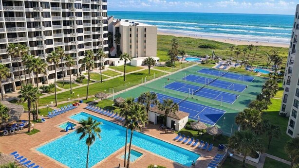 Un hotel con piscina, canchas de tenis y vista al mar.