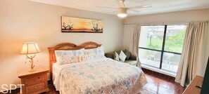 Una camera da letto con un letto, un comodino, una lampada e un'ampia finestra con tende.