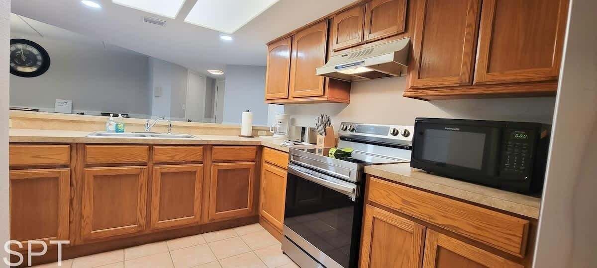 A kitchen with wooden cabinets, a stainless steel stove, a microwave, and a sink.