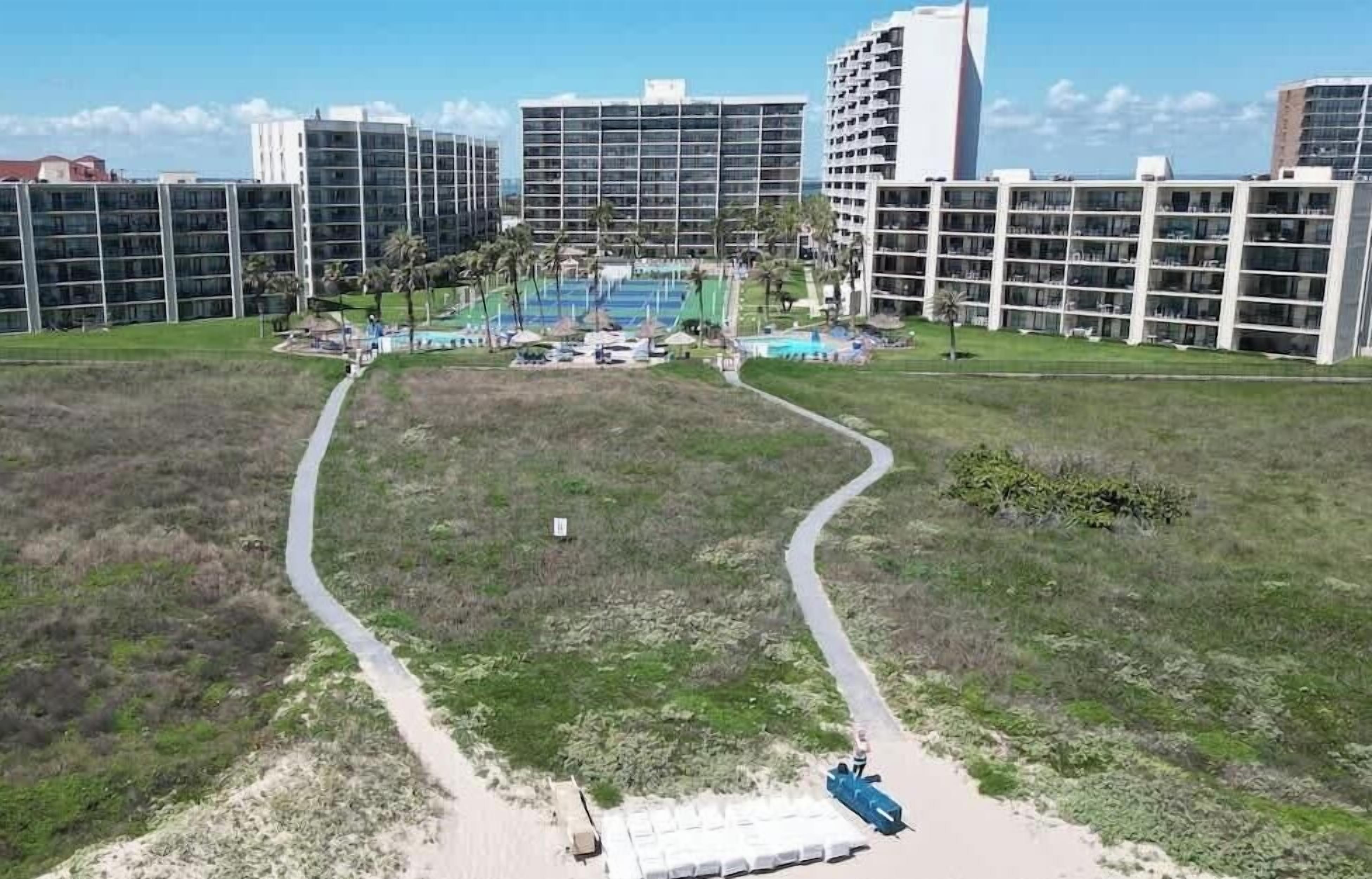 Un moderno complejo hotelero con múltiples edificios altos, un patio central con piscina y un césped bien cuidado.