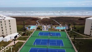 Un complejo de canchas de tenis con varias canchas, un área de piscina y vistas a la playa y el océano.