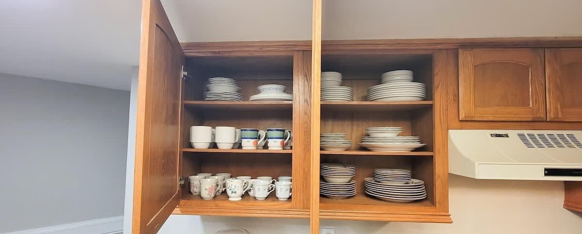 A kitchen with wooden cabinets, shelves with plates and cups, and a built-in oven.