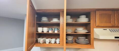 A kitchen with wooden cabinets, shelves with plates and cups, and a built-in oven.