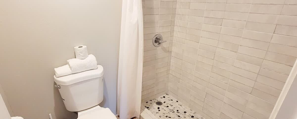 Un baño con inodoro, ducha y paredes de cerámica.