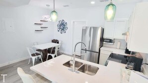 Una cocina moderna con armarios blancos, un refrigerador de acero inoxidable, un lavamanos doble e iluminación colgante.