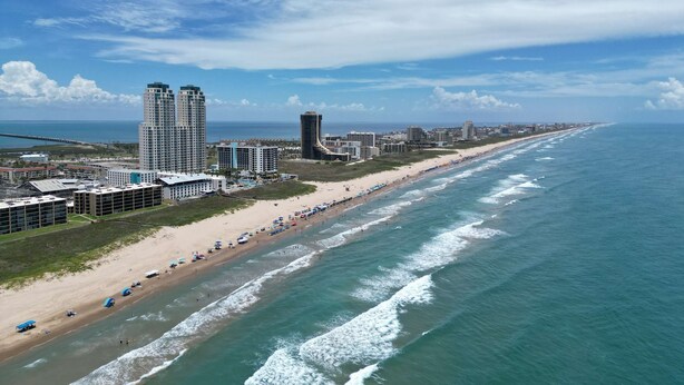 Un paisaje urbano costero con una playa extensa, edificios altos y cielo despejado.