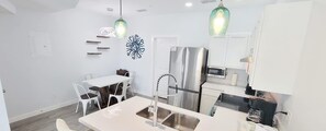 A modern kitchen with white cabinetry, a stainless steel refrigerator, a double sink, and pendant lighting. - Villas De Laguna 4 3 Bedroom Townhouse (South Padre Island)