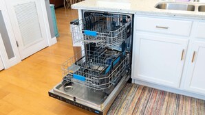 An open dishwasher in a kitchen with white cabinets and a striped rug.