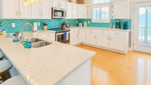 A modern kitchen with white cabinets, a teal backsplash, a stainless steel sink, and a built-in oven.