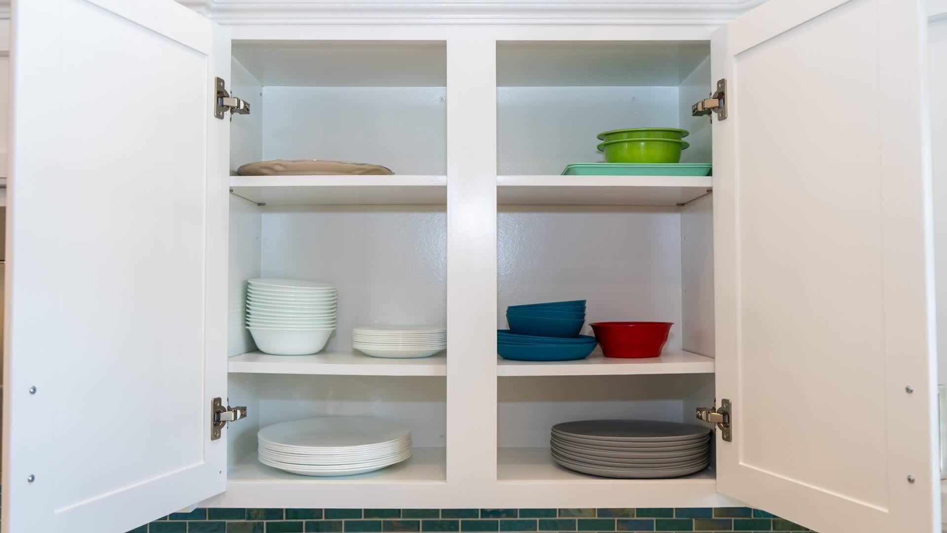 Un mueble blanco con cuatro estantes, cada uno con pilas de platos y tazones de varios colores.