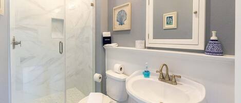 A bathroom with a glass shower enclosure, a toilet, a sink with a mirror above, and a blue decorative item on the sink.