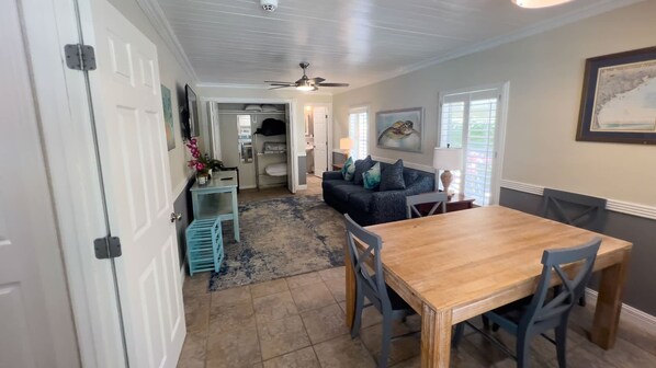 A dining area with a wooden table and chairs, a blue sofa, and a kitchen in the background. - 121 Snapper By The Sea 4 Bedroom Home (South Padre Island)