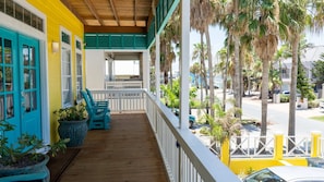 A wooden porch with teal chairs and potted plants, overlooking a street with palm trees and parked cars. - 121 Snapper By The Sea 4 Bedroom Home (South Padre Island)