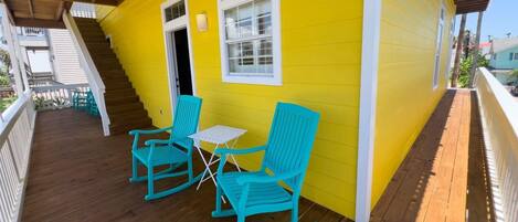 A yellow house with a wooden porch, two rocking chairs, and a small table.