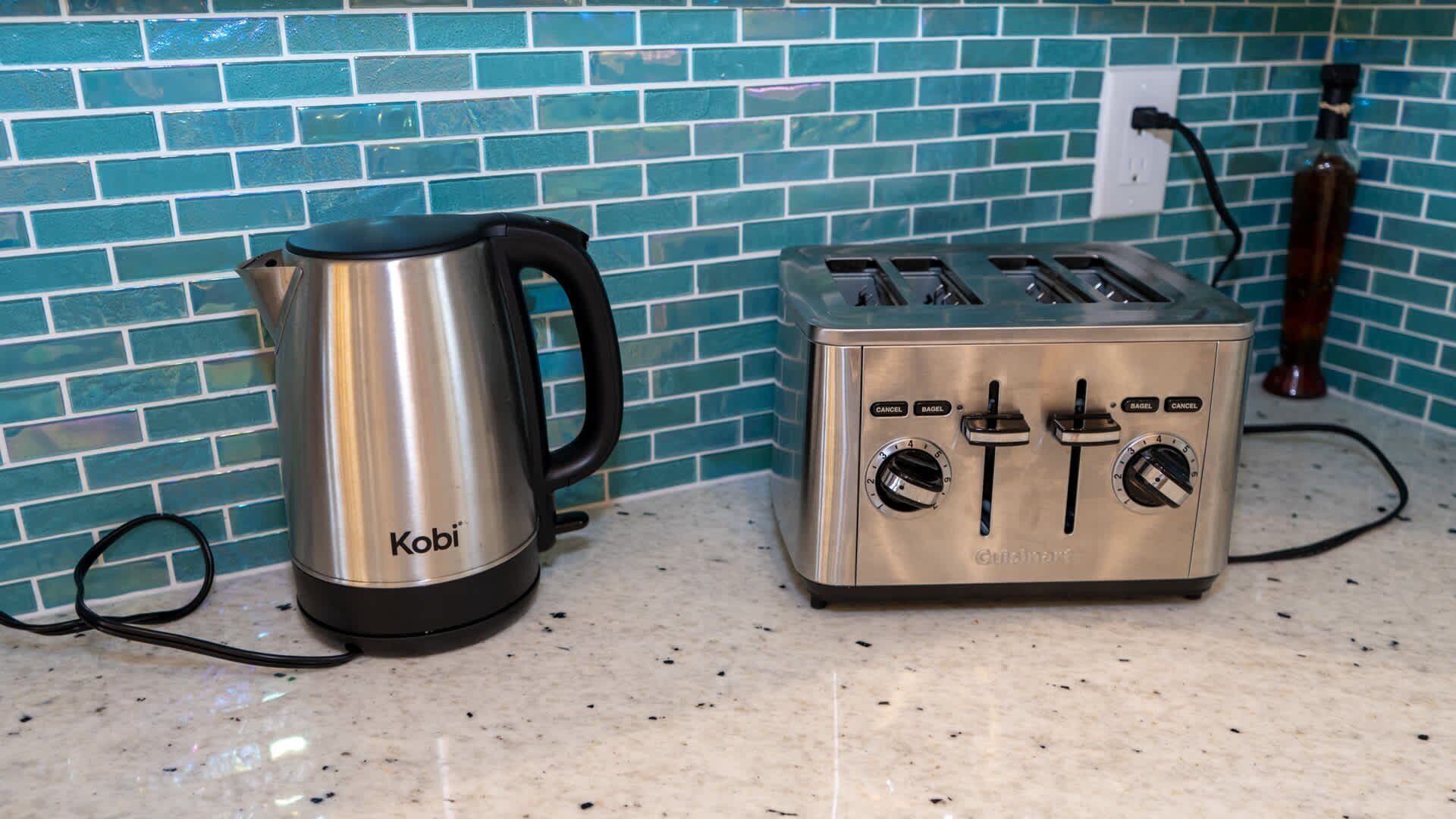 Ein Edelstahl-Wasserkocher und ein Toaster stehen auf einer Küchenarbeitsplatte mit Fliesenwand.