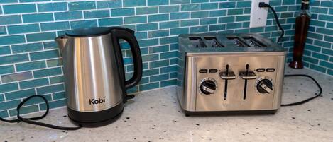 Ein Edelstahl-Wasserkocher und ein Toaster stehen auf einer Küchenarbeitsplatte mit Fliesenwand.