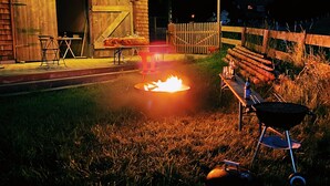 An outdoor patio area with a fire pit, a grill, and a wooden fence. - Beautiful, renovated 100 sqm vacation apartment in a former farmhouse in the Allgäu (Maierhöfen)