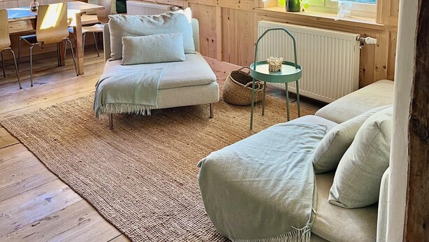 A cozy room with wooden walls, a sofa, a dining table with chairs, and large windows. - Beautiful, renovated 100 sqm vacation apartment in a former farmhouse in the Allgäu (Maierhöfen)