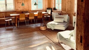 A rustic wooden interior with a dining area, sofa, and large windows. - Beautiful, renovated 100 sqm vacation apartment in a former farmhouse in the Allgäu (Maierhöfen)
