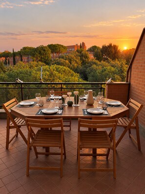 A wooden dining table set for four with plates, cutlery, and glasses, overlooking a lush garden and buildings in the distance. - Spacious Vatican Apartment near Metro A with Private Terrace – Sleeps 8, Parking (Roma)