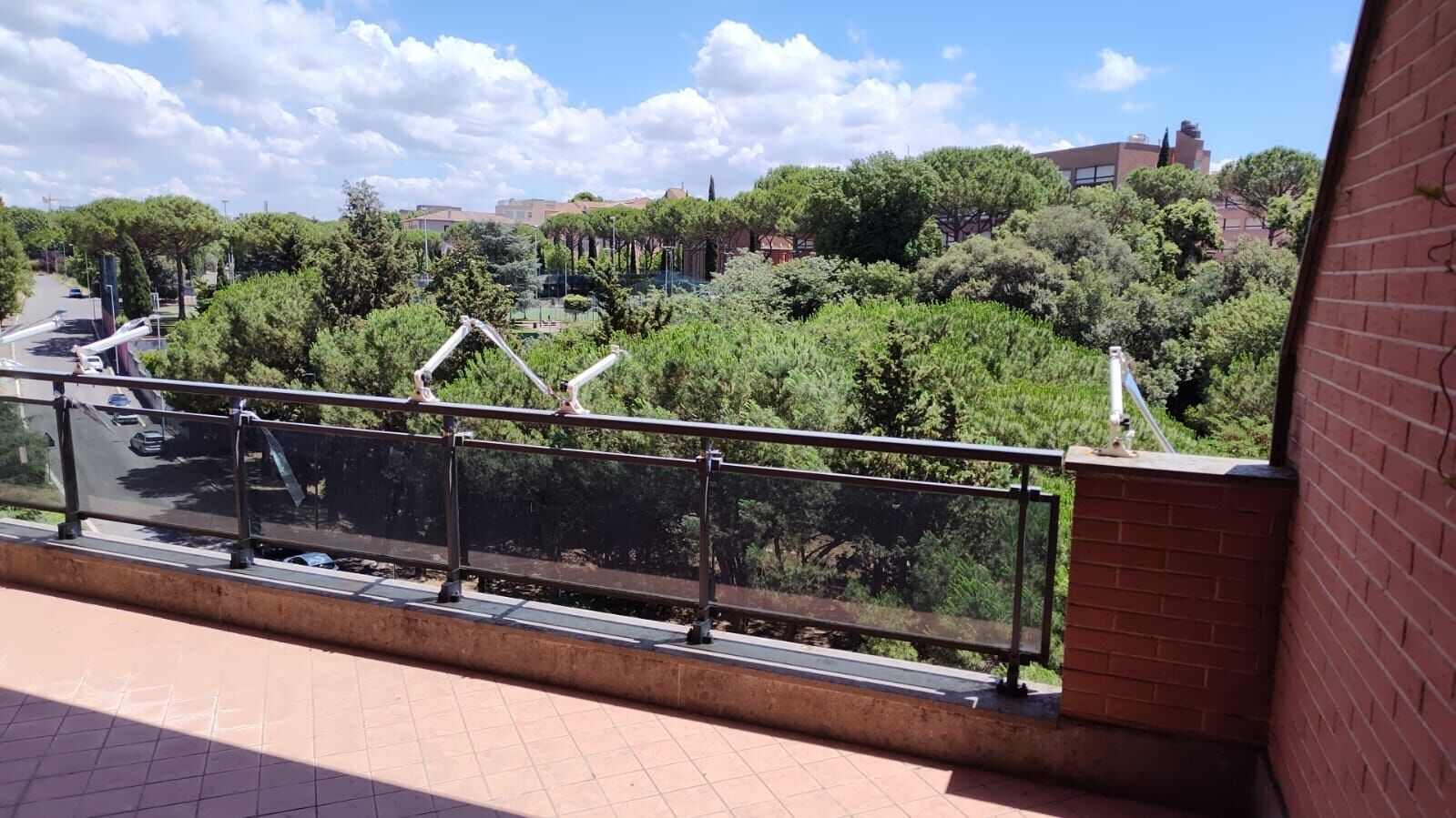 Un balcone con ringhiera in metallo affaccia su una strada e del verde.