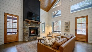 Ein geräumiges Wohnzimmer mit Kamin aus Stein, einer Ledersofa und großen Fenstern.