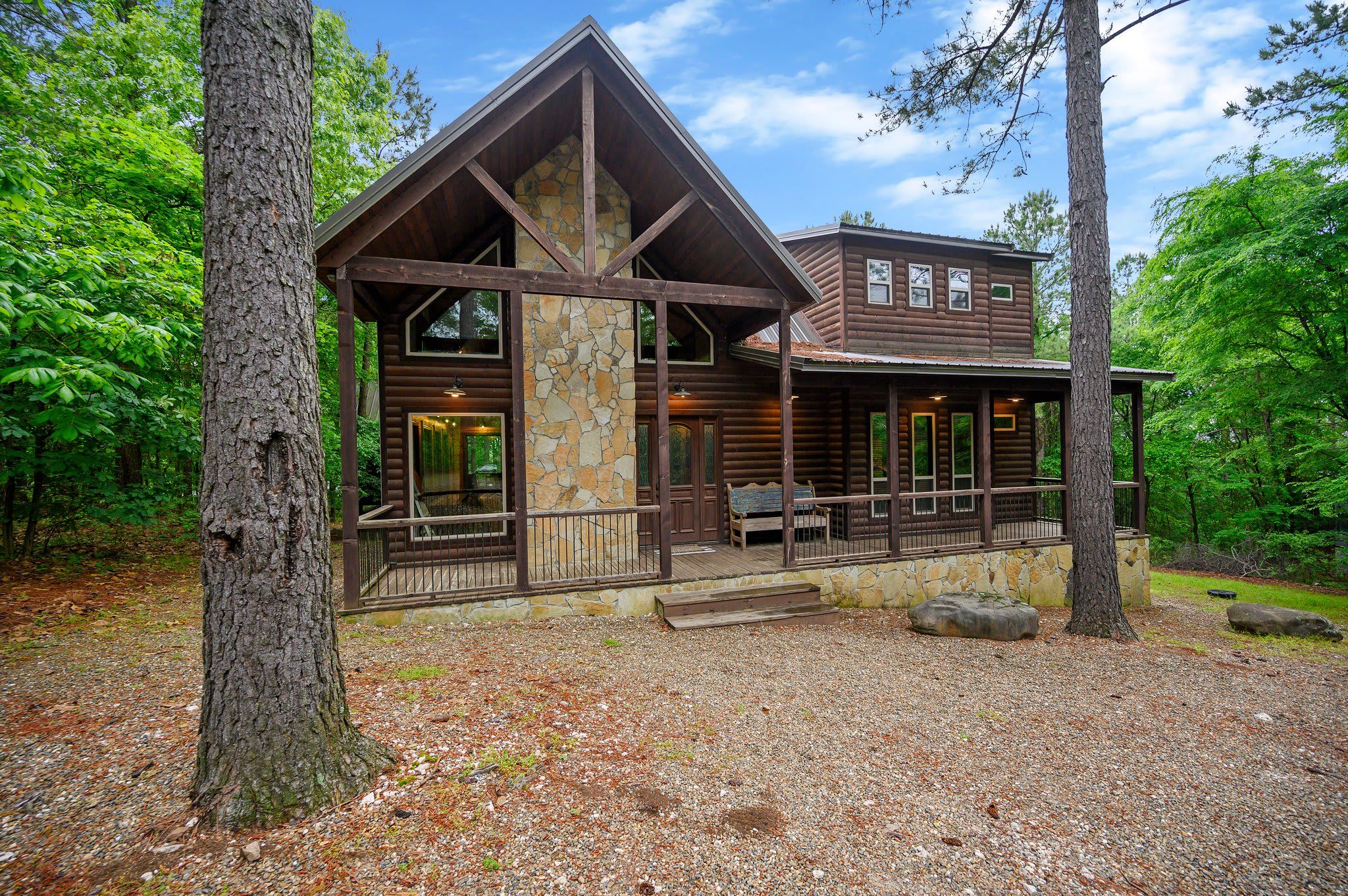 A rustic log cabin with a stone chimney, large windows, and a porch.