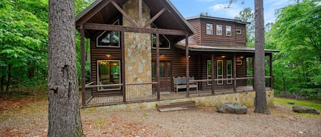 A rustic log cabin with a stone chimney, large windows, and a porch.