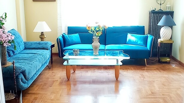 Een woonkamer met een blauwe zithoek, een houten visgraatvloer en een schilderij aan de muur.