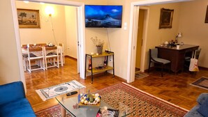 Een woonkamer met een televisie, een eettafel, stoelen en een salontafel met decoratieve objecten.