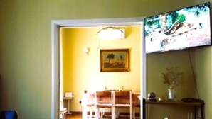 Een woonkamer met houten vloer, een aan de muur bevestigde televisie en een schilderij.