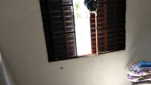 A room with tiled flooring, a window with wooden shutters, and a bed with a floral bedspread. - Hospedagem  (Sao Gabriel)