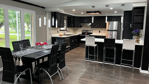 A modern kitchen with black cabinets, stainless steel appliances, and a dining area with black chairs and a striped tablecloth.