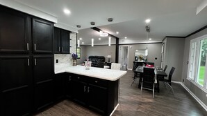 A modern kitchen with dark cabinetry, a marble countertop, and a dining area with a black table and chairs.