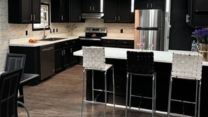 A modern kitchen with dark cabinetry, stainless steel appliances, and a central island with bar stools.