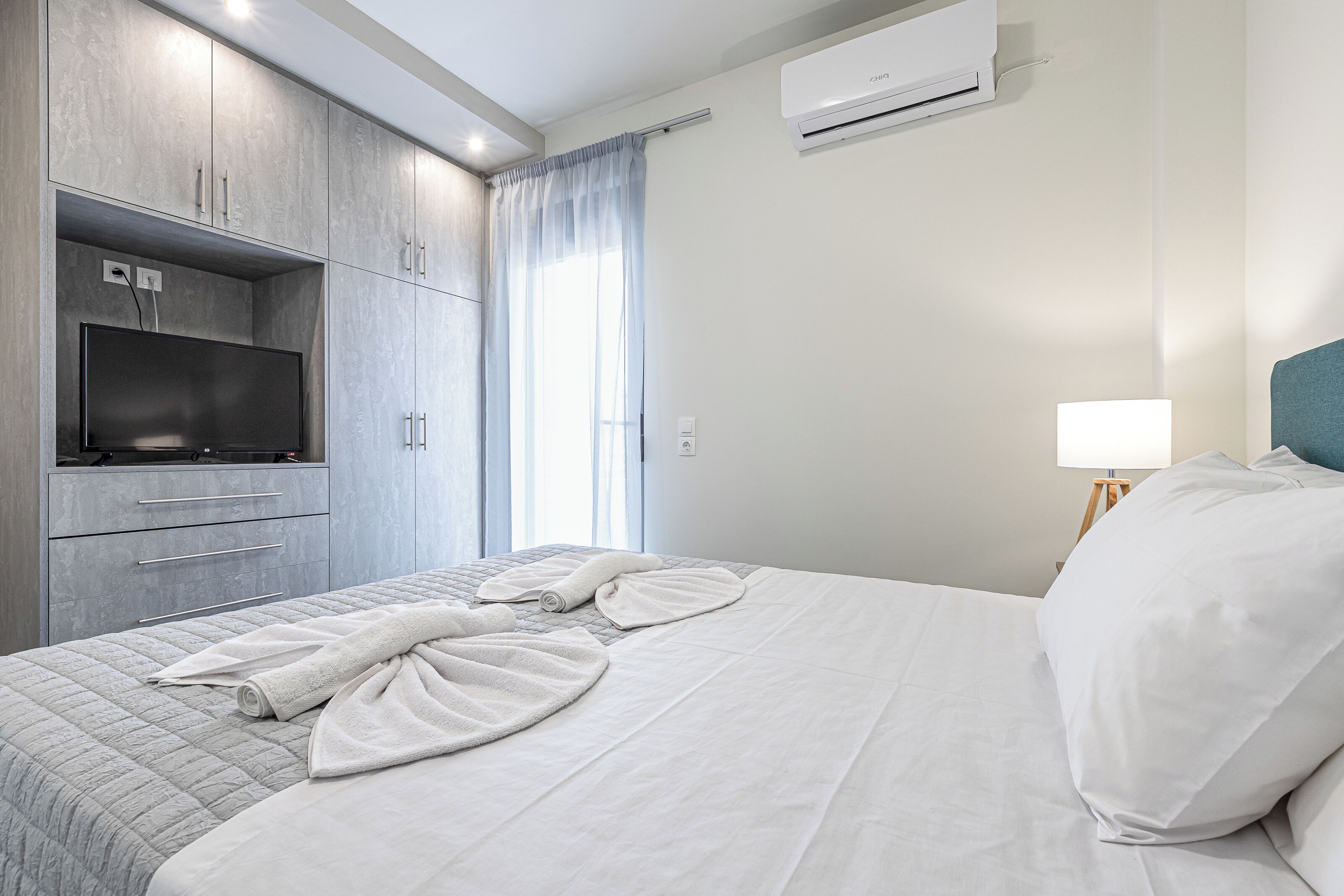 A modern hotel room with a bed, a TV, a wardrobe, and an air conditioner.