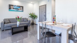 A modern living room with a grey sofa, a coffee table, and a dining area with a wooden table set for two.