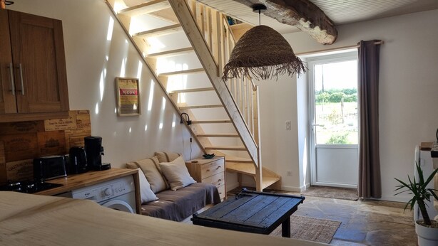 A cozy living room with a wooden staircase, a sofa, a coffee table, and a hanging light fixture. - Le gite d'URYA - Ideal for a romantic vacation (Saint-Mard)