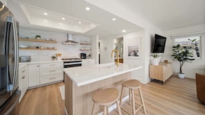 A modern kitchen with white cabinetry, a central island with stools, a stainless steel refrigerator, and a wooden floor.