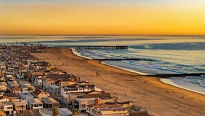 A coastal town with a long pier extending into the sea, a sandy beach, and residential buildings along the shore.